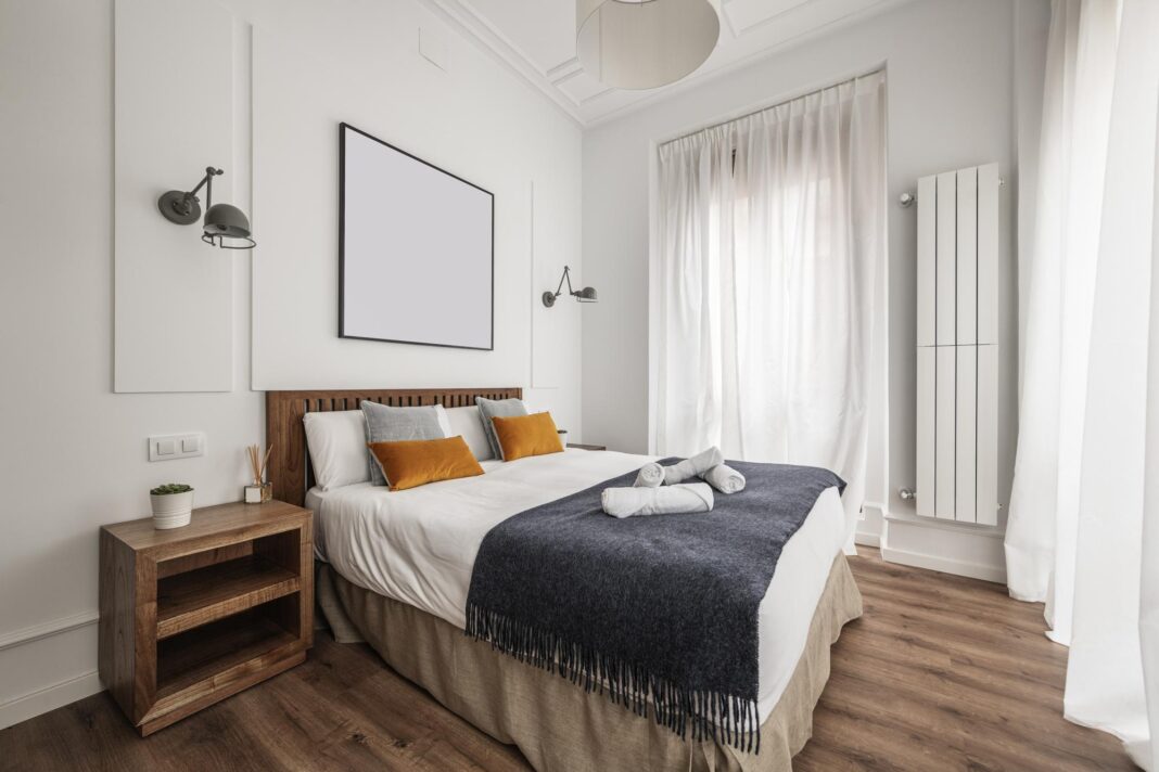 Double bedroom with king size bed side tables and wooden headboard and white cotton curtains in vacation rental apartment