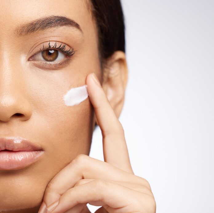 Half woman and sunscreen on face for skincare and dermatology in studio background Calm girl and apply lotion moisturizer in portrait for healthy glow or self care in beauty with cosmetics