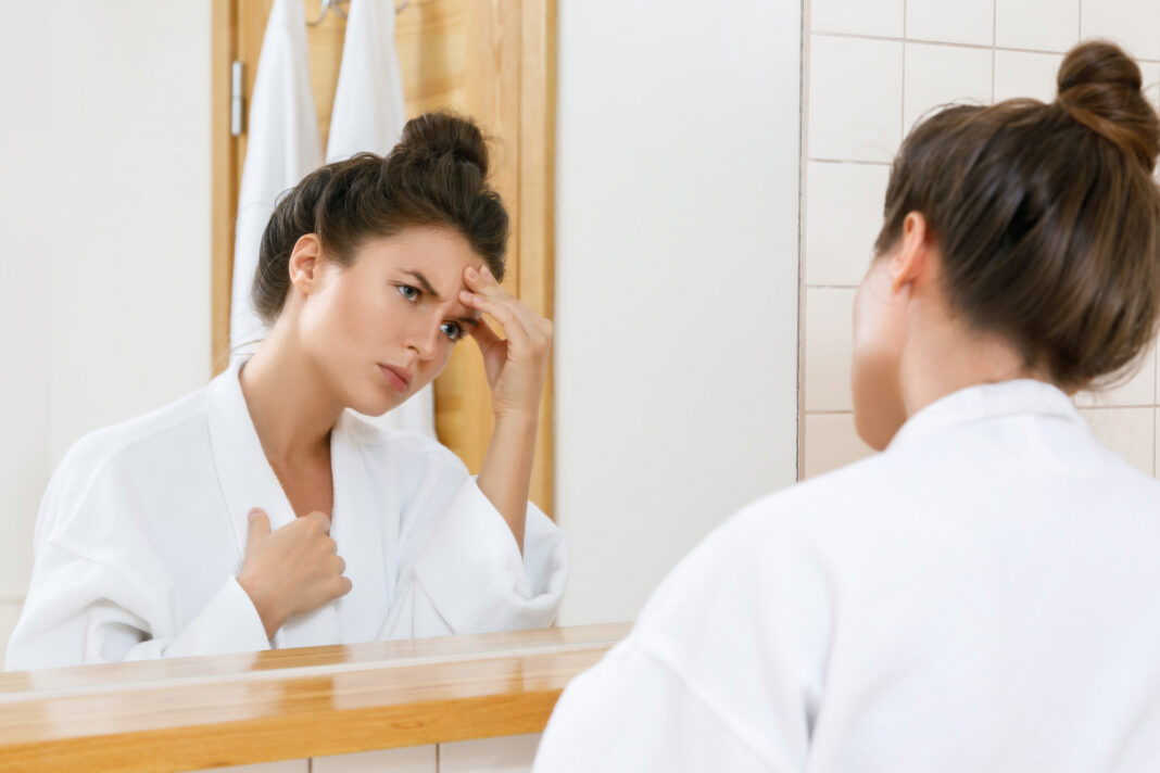 Woman with a headache looking into the mirror
